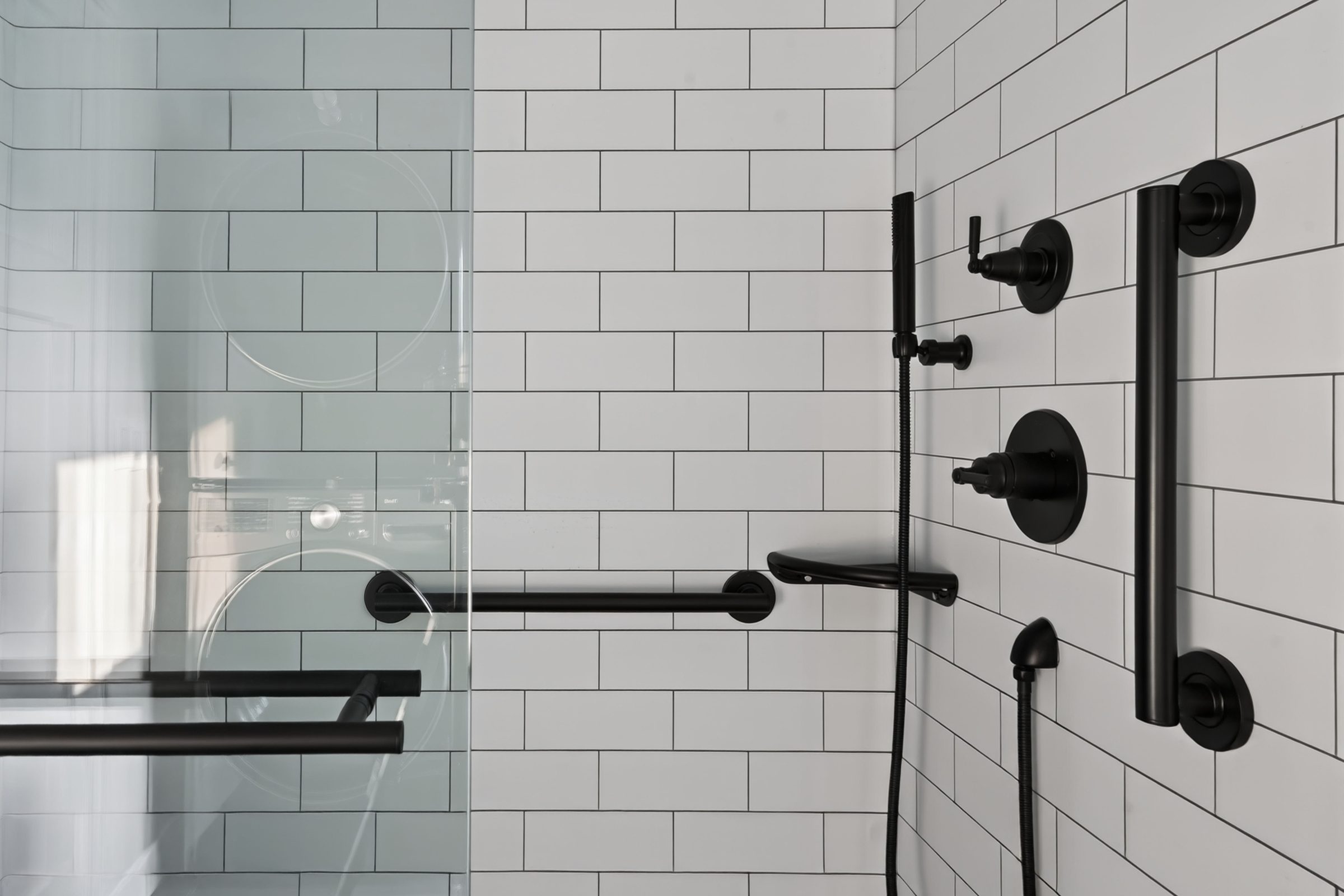 Matte black shower valve, handheld head, and grab bars against white subway tile — aging-in-place ADU, Madison WI
