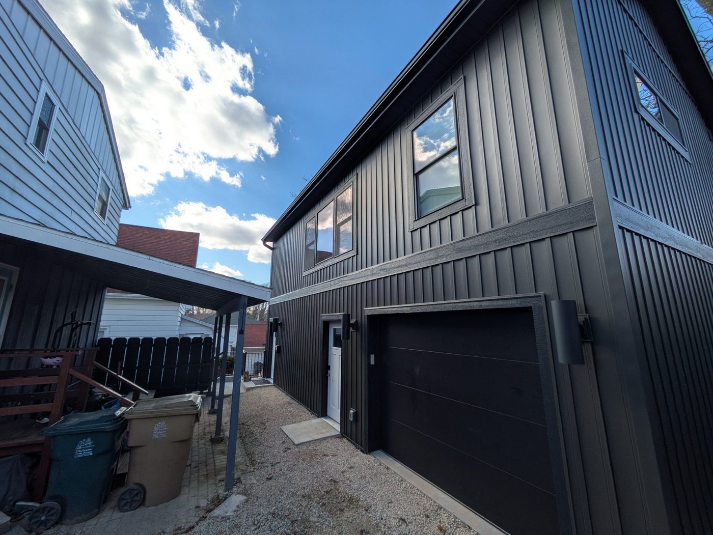 Completed garage ADU — black garage door and white ADU entry door, dark board and batten siding, Henry Vilas Madison WI